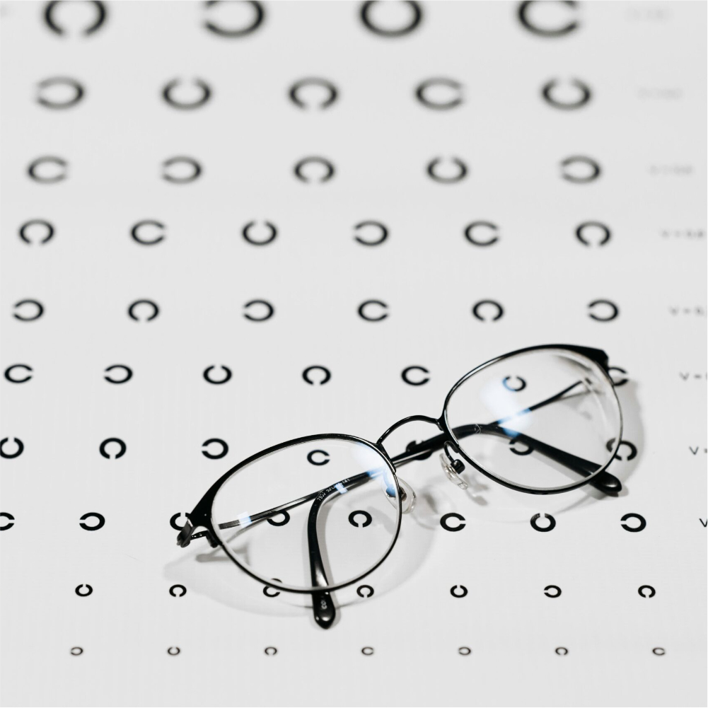 Gafas de montura negra sobre un optotipo para un examen visual completo.