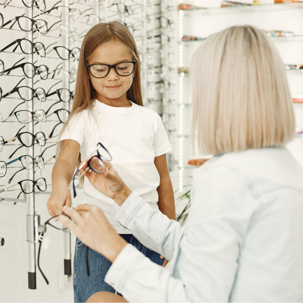 Niña probándose gafas con una especialista en terapia visual en una óptica.